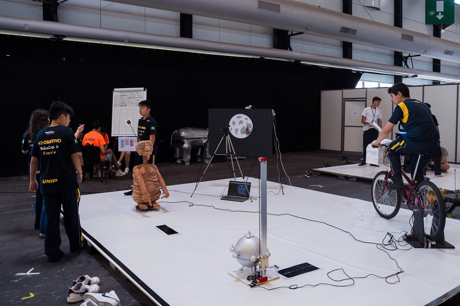 Una presentación de RoboCupJunior OnStage con una figura de E.T., una luna proyectada y una bicicleta que genera electricidad a pedales.